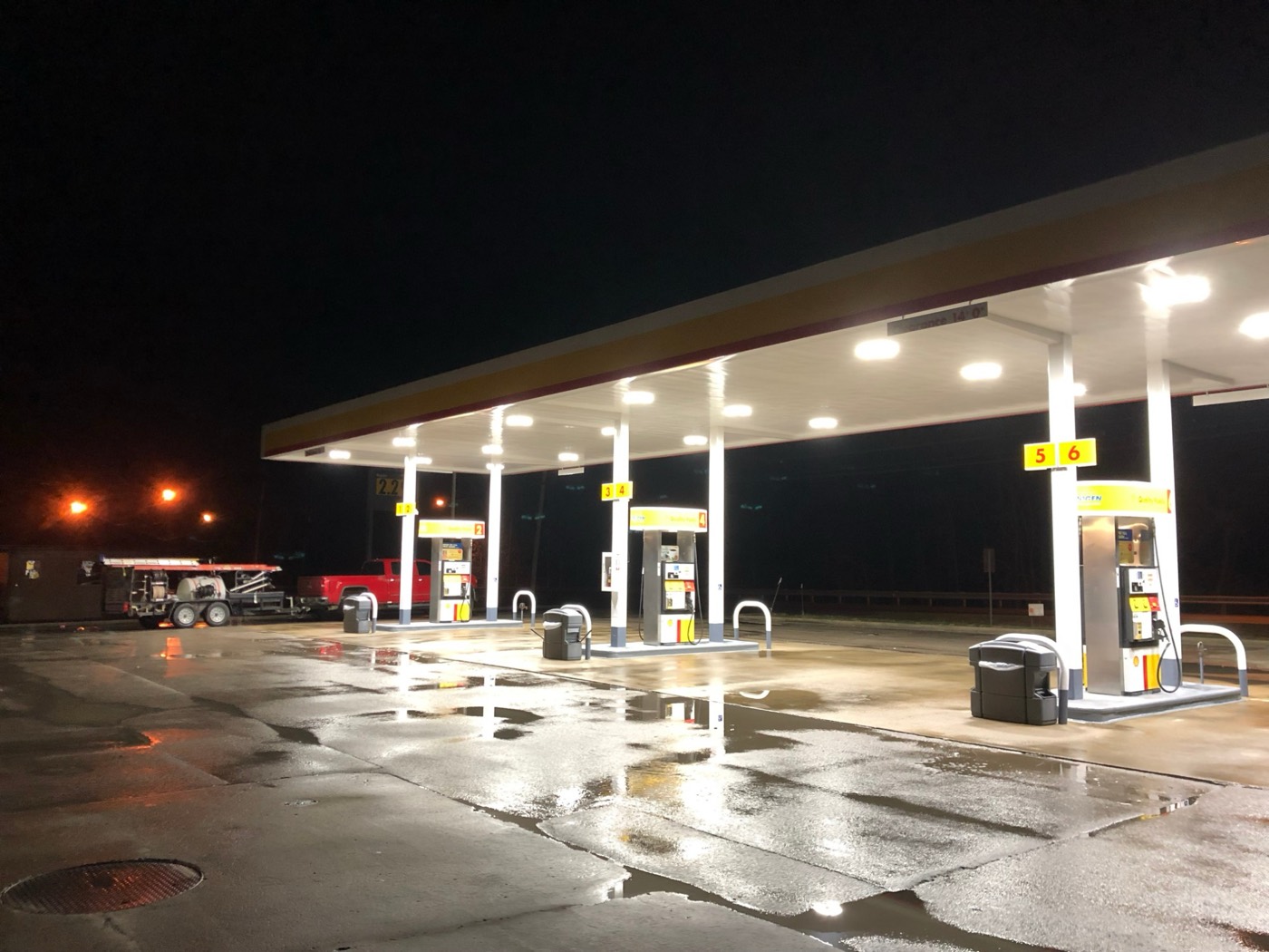A gas station canopy and pumps freshly washed at night, with the Pressures ON rig parked nearby